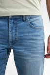 Detail van de voorkant van een lichtblauwe jeans met een lichte wassing, zichtbare stiksels en zakdetails.