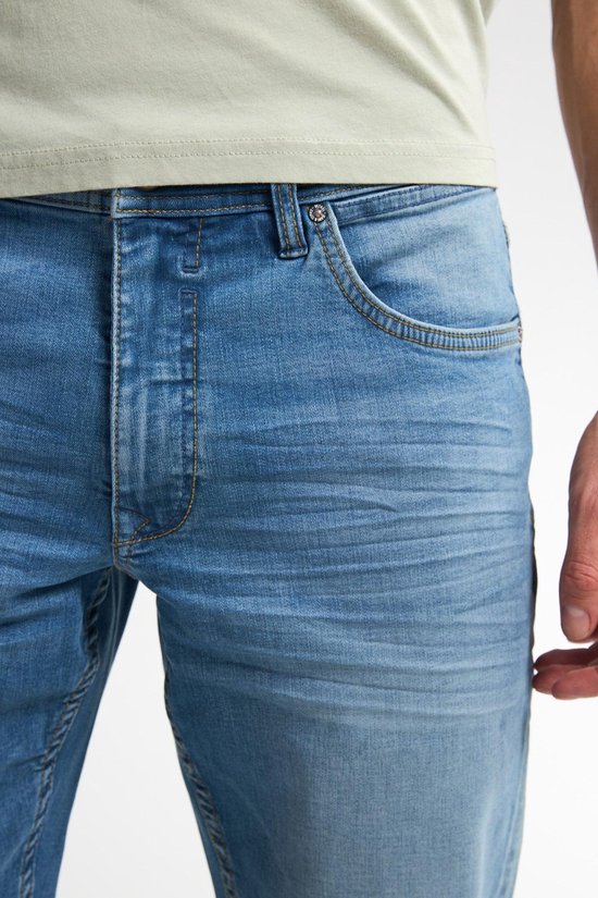 Detail van de voorkant van een lichtblauwe jeans met een lichte wassing, zichtbare stiksels en zakdetails.
