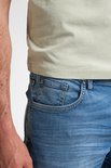 Detail van de zijkant van een lichtblauwe jeans met een lichte wassing en zichtbare stiksels.