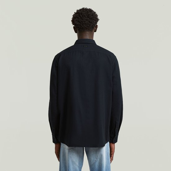Man, van achteren, draagt een donkerblauw regular fit overhemd en lichte jeans.