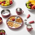 Roze serviesset met een verdeeld bord, kom, beker en bestek, gevuld met snacks en fruit.