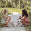 Twee meisjes met poppen in roze kinderwagens in een buitenomgeving.