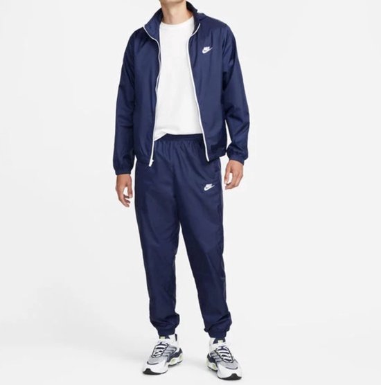 Donkerblauw trainingspak van Nike met witte rits en logo, gedragen met wit T-shirt.