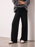 Zwarte wijde joggingbroek met trekkoord en witte sneakers.