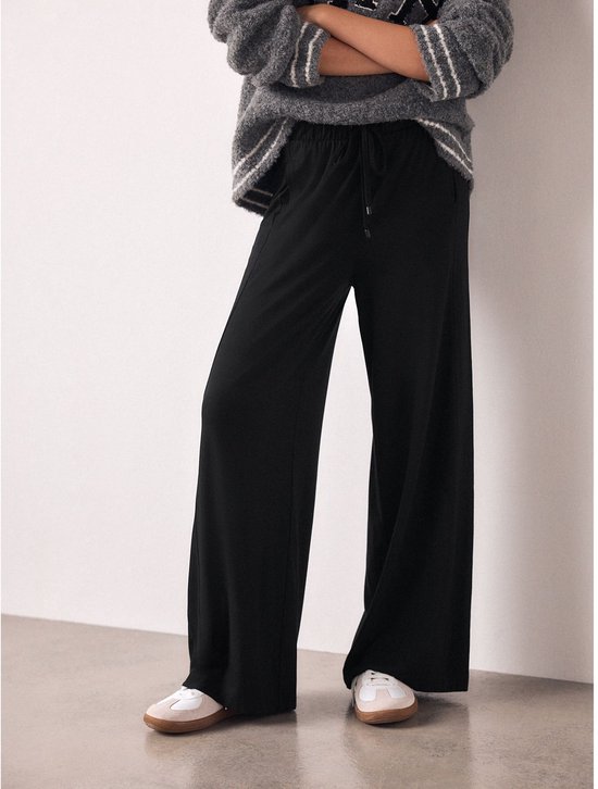 Zwarte wijde joggingbroek met trekkoord en witte sneakers.