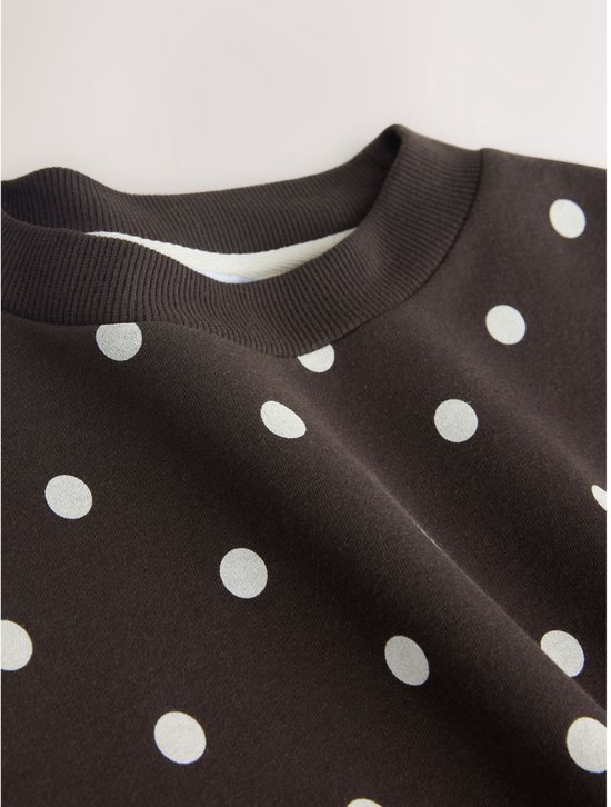 Close-up van de halslijn van een donkerbruine sweater met witte polkadotprint.