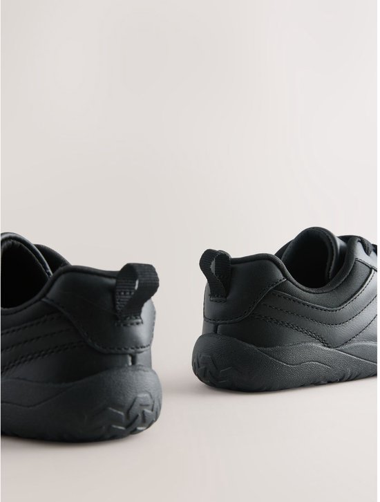 Achterkant van zwarte leren veter-sneakers, met lus aan de hiel en een golfachtig profiel op de zolen.
