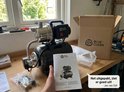 Hand die een handleiding vasthoudt met een afbeelding van een waterpomp, naast een uitgepakte zwarte en zilverkleurige waterpomp.