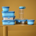 Stapel lichtblauwe Mepal lunchboxen en een waterfles met blauwe doppen.