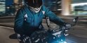 Een motorrijder in een blauwe jas en helm rijdt 's nachts door de stad, met een Insta360 camera gemonteerd op de motor.