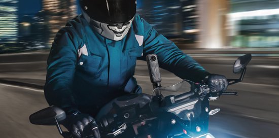 Een motorrijder in een blauwe jas en helm rijdt 's nachts door de stad, met een Insta360 camera gemonteerd op de motor.