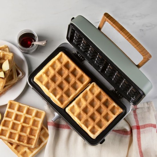 Groene wafelijzer met twee gebakken wafels en extra wafels op een bord.