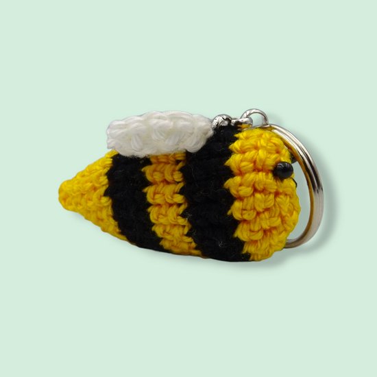 Gehaakte bijensleutelhanger met gele en zwarte strepen en witte vleugels.