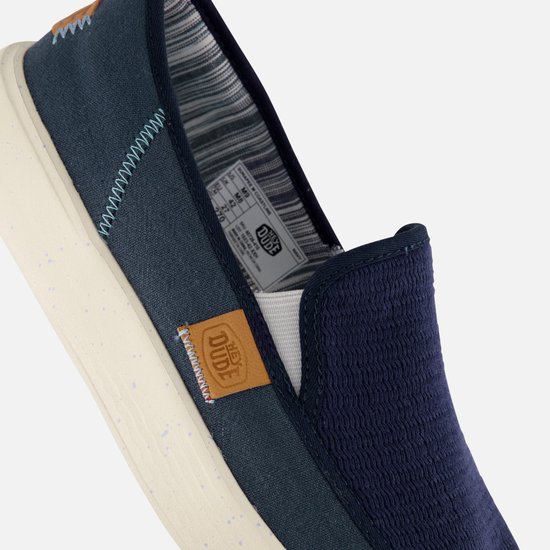 Détail d'un mocassin HEYDUDE bleu marine avec accent textile et logo.