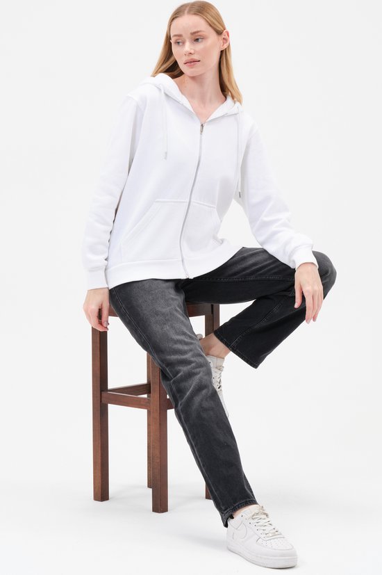 Model zit op krukje met witte hoodie en zwarte jeans.