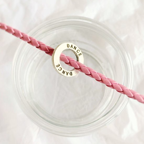 Roze gevlochten leren armband met zilverkleurige ring met de tekst 'DANCE'.