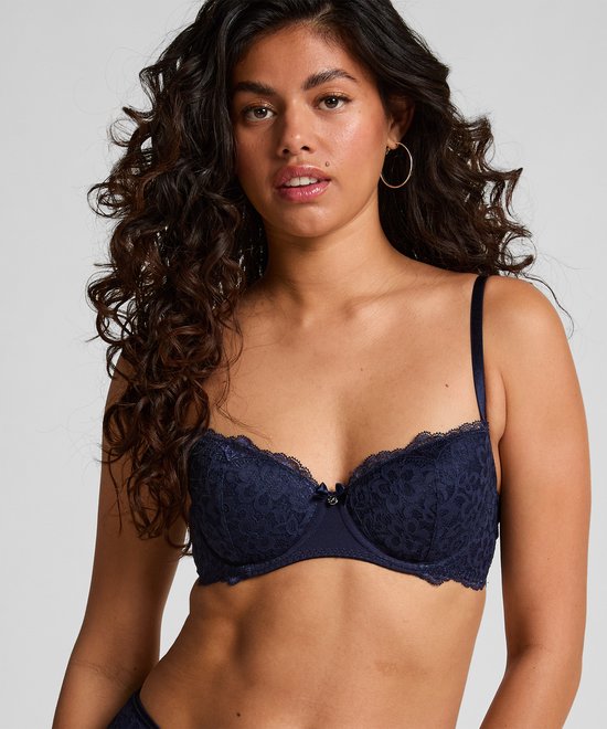 Model met krullend haar draagt een donkerblauwe kanten beugelbeha.