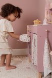 Kind met creme kleding draagt bloemen ovenwant en draait aan knop van roze speelgoedkeuken.