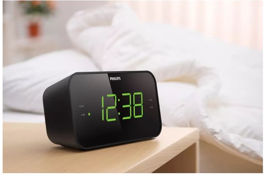 Zwarte Philips wekkerradio met groene digitale cijfers op een houten nachtkastje.