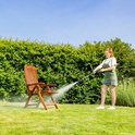 Een vrouw met tuinbroek reinigt een houten stoel met een hogedrukreiniger.