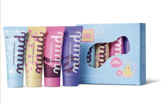 Vier buisjes natuurlijke deodorant in de kleuren lichtblauw, geel, roze en paars, naast een blauw doosje met een uitgesneden venster dat dezelfde buisjes toont. Tekst op buisjes: 'nuud natural deodorant'.