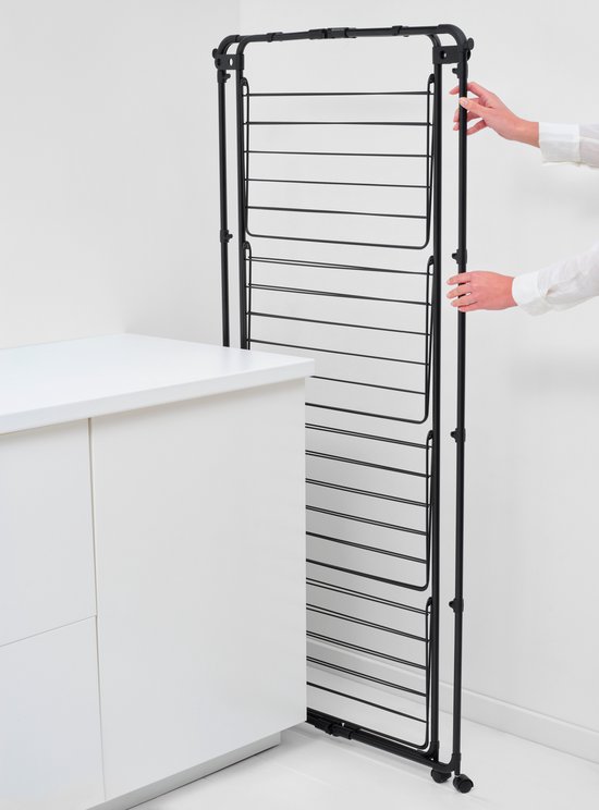 Zwarte, rechtopstaande droogtoren met veel drooglijnen, die door handen wordt ingeklapt bij een witte keuken.
