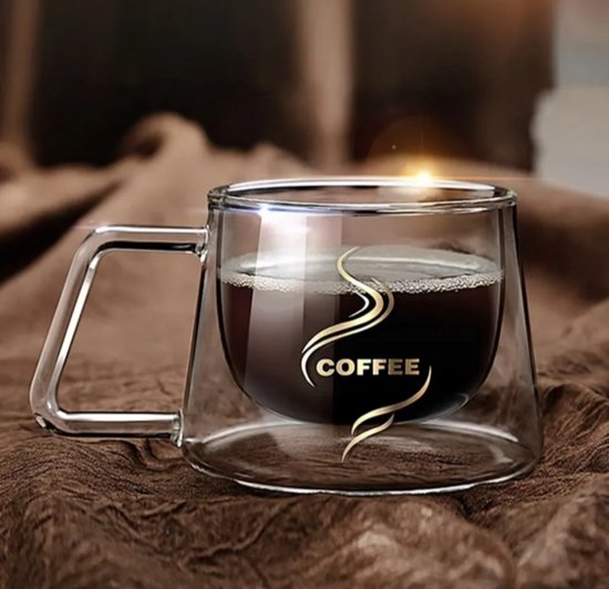Dubbelwandige koffiemok van glas met handvat, gevuld met zwarte koffie en schuim, op bruine stof.