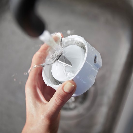 Hand spoelt blenderonderdeel met mesjes onder de kraan.