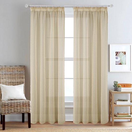 Twee beige vitrage gordijnen hangen voor een raam, met een stoel ernaast.