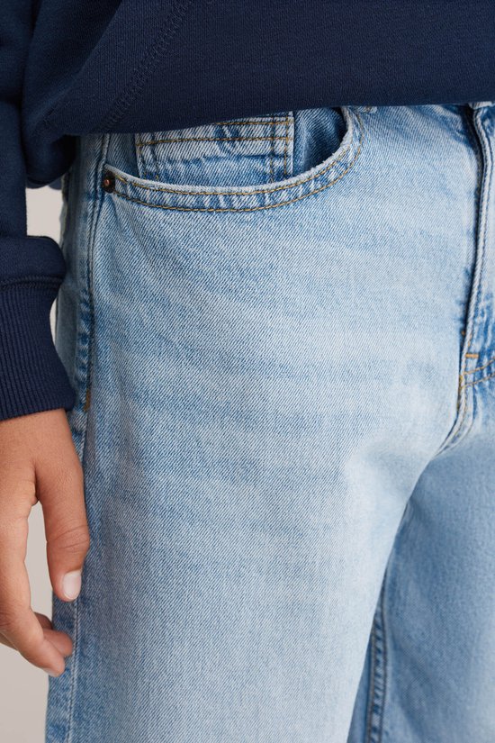 Close-up van een jongen in een lichte spijkerbroek met een donkere hoodie.
