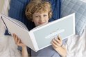 Jongen ligt op bed met een open mintgroen schoolfotoboek in handen. De kaft heeft een patroon van driehoekjes.