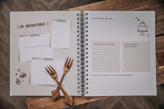 Een open ringband-planner met twee gouden vorken erop. De tekst 'DE BRUIDSTAART' is zichtbaar.