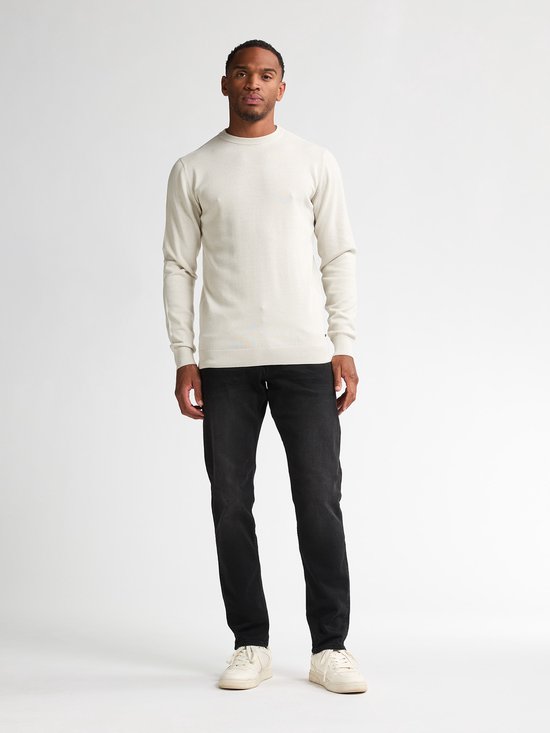 Man met beige trui en zwarte jeans, van voren gezien.