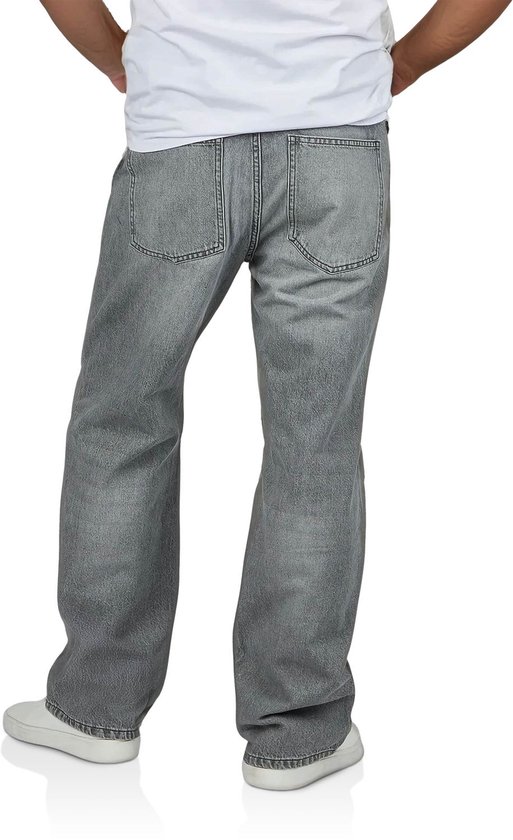Achterkant van een man met een losse grijze spijkerbroek, witte t-shirt en witte sneakers.