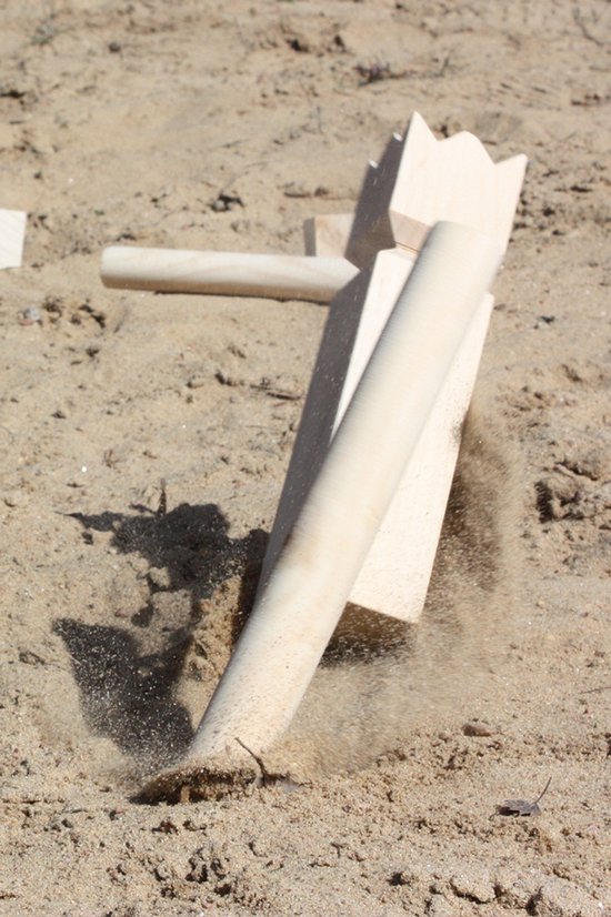 Een werpstok raakt een houten Kubb skittle, waardoor zand opspuit.