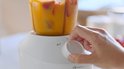 Hand draait aan de knop van een witte Philips blender, de blenderbeker bevat een oranje drank met stukjes fruit.
