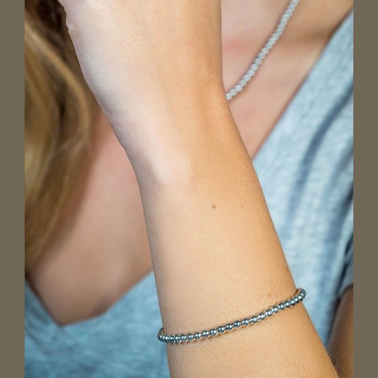 Arm met een zilverkleurige armband van kleine bolletjes, gedragen met een grijs shirt.