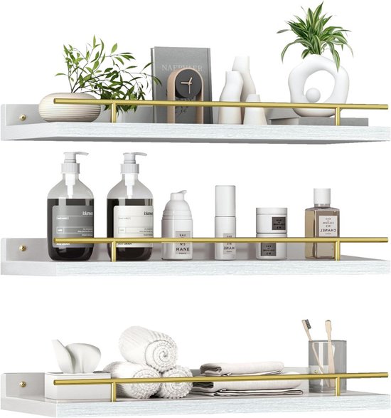 Drie witte wandplanken met gouden rails, gevuld met decoratie, zeepflessen en handdoeken.