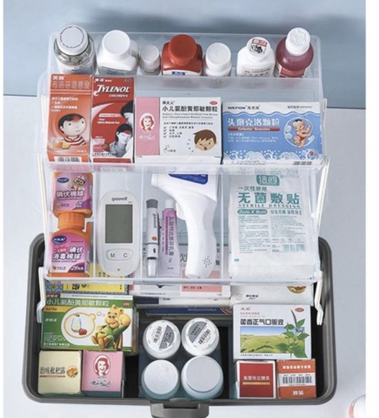 Gevulde donkergrijze medicijnkist met transparante uitklapbare bakjes, met medicijnen, thermometer, spuiten.