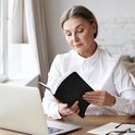 Grijshaarige zakenvrouw in wit overhemd leest in zwart notitieboek met slot-icoon op tafel.