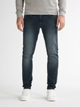 Man met donkerblauwe slim fit jeans, licht vervaagd aan de voorkant, met witte sneakers.