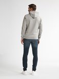 Man van achteren gezien, draagt een grijze hoodie en blauwe slim fit jeans. Witte sneakers.