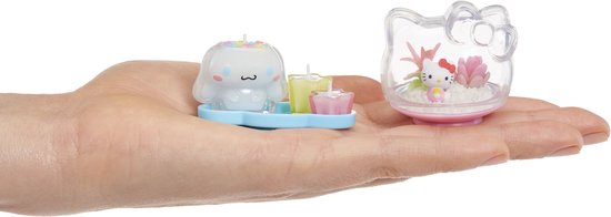 Hand die miniatuur figuren vasthoudt van Cinnamoroll en Hello Kitty in terrarium.