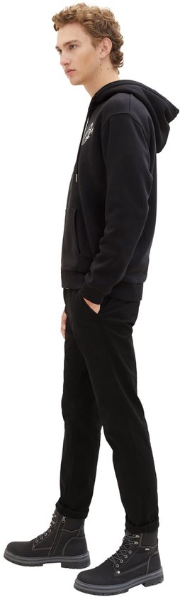 Man in zwarte skinny jeans met zwarte hoodie en grijze boots.