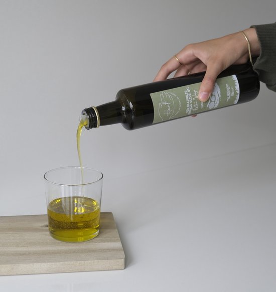 Hand met gouden armband schenkt Hant biologische olijfolie uit een glazen fles in een glas.