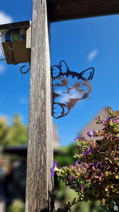 Zwart metalen kattenfiguur dat om een houten paal kijkt, met roestige accenten, grote ogen en speelse oren.