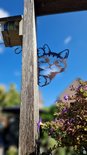 Zwart metalen kattenfiguur dat om een houten paal kijkt, met roestige accenten, grote ogen en speelse oren.