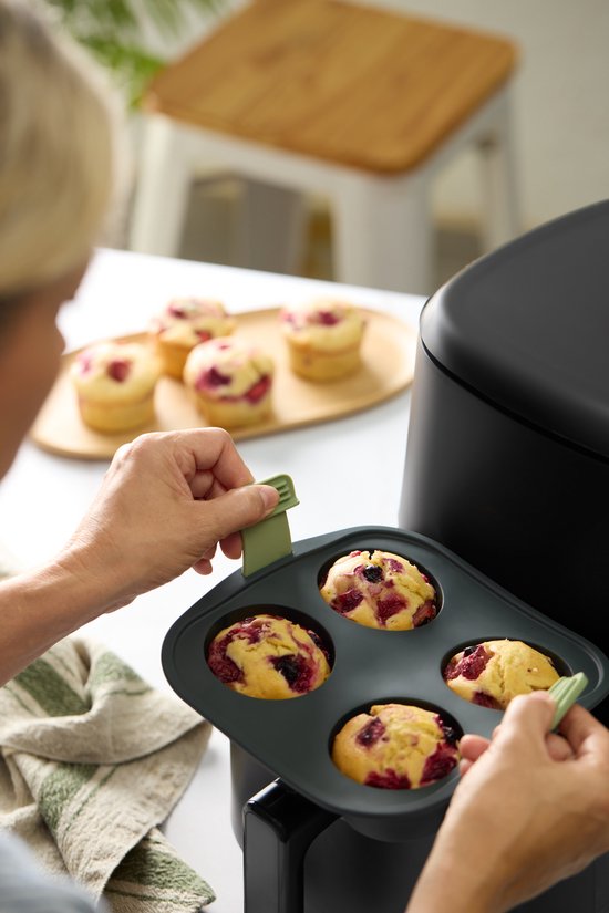 Handen pakken een donkergrijze muffinvorm met 4 bessenmuffins uit een heteluchtfriteuse.