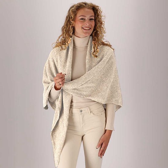 Model draagt een beige gebreide omslagdoek over een beige coltrui en broek.