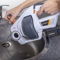 Wit/grijs gereedschap met oranje accenten, in gebruik bij een aanrecht.